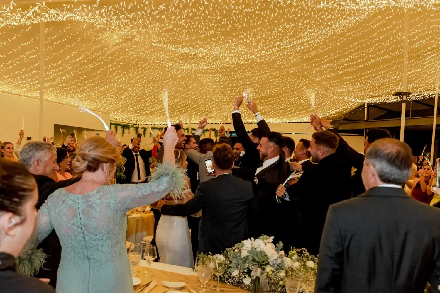 Invitados bailando y agitando servilletas bajo la carpa iluminada