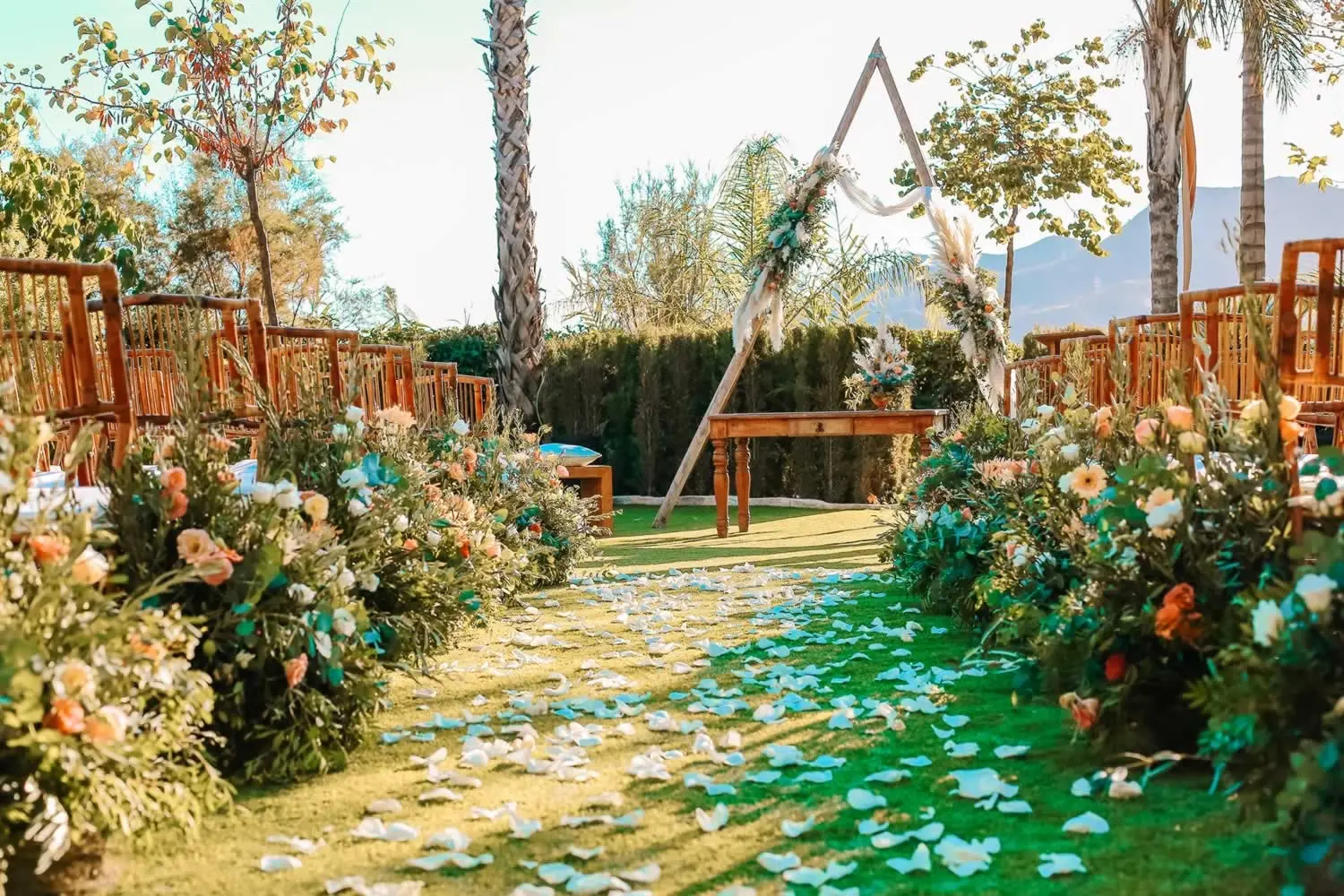 Un pasillo de flores y pétalos lleva a un arco de madera entre palmeras