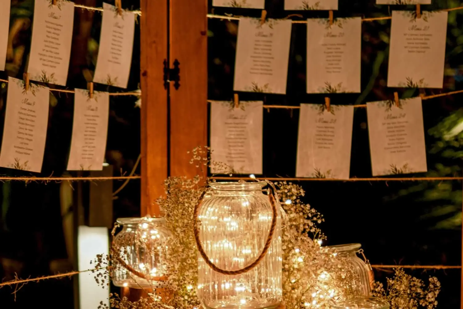 El seating: tarjetas de mesa colgadas con pinzas y farolillos de cristal con luces