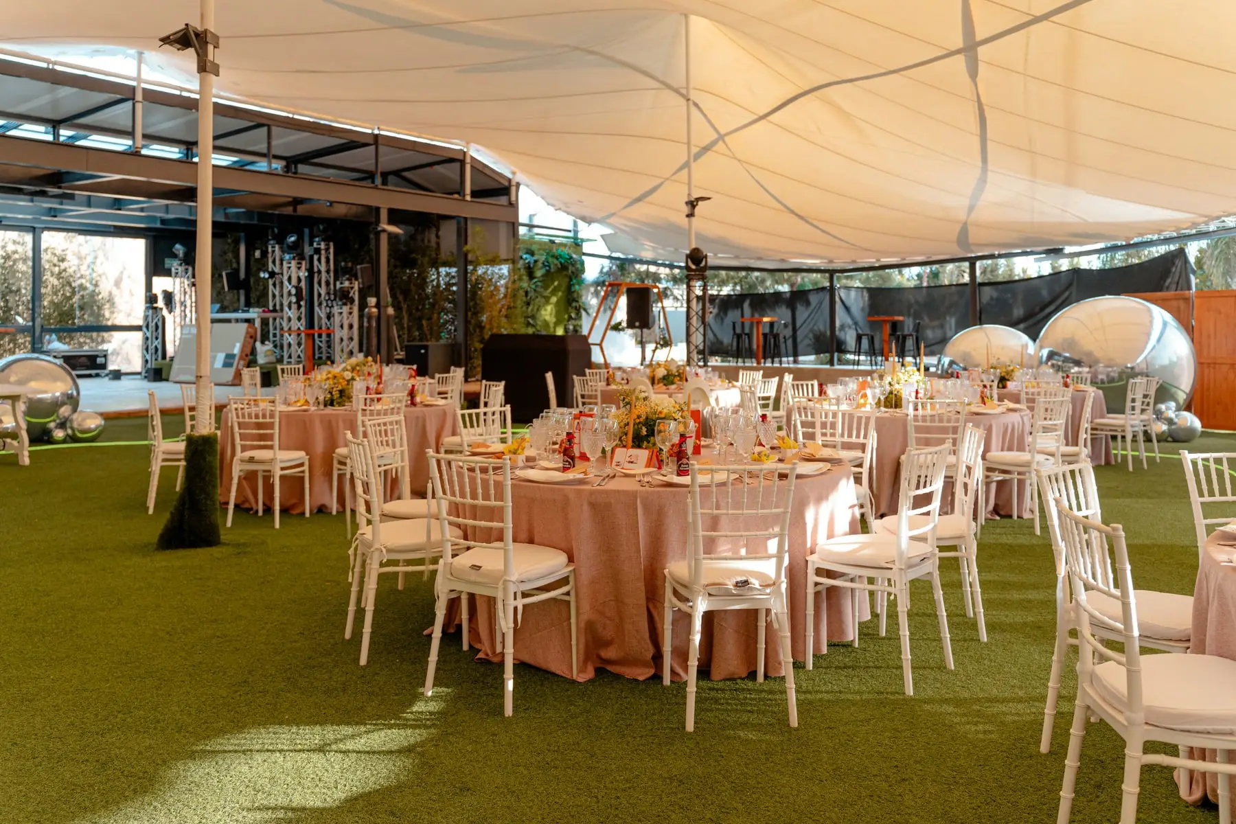 Mesas con mantel rosa bajo la carpa, abierta al jardín